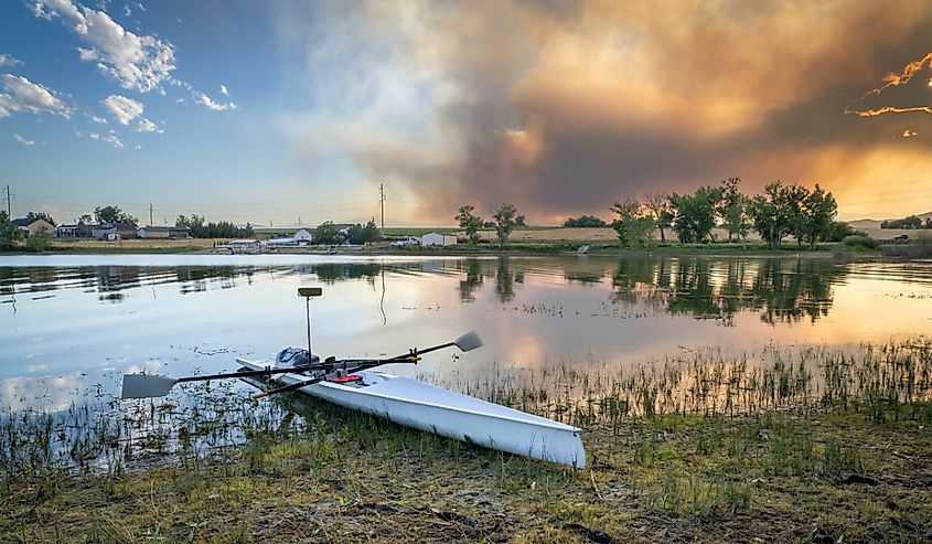 Rowing shell at a shore of Boyd Lake near Loveland, Colorado, with a smoke plume from Alexander Mountain fire as seen at sunset,