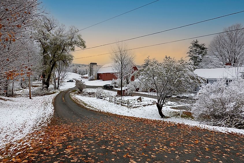 Autumn leaves blanket a highway while snow dusts the surrounding countryside in Walpole, New Hampshire