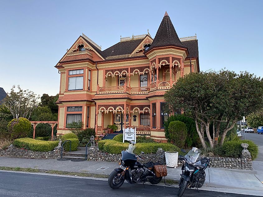 A pink and beige mansion with gingerbread trim with two motorcycles parked out front.