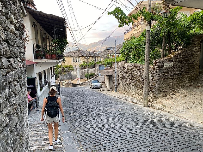 A woman walks down a cobblestone street in an ancient mountain town.