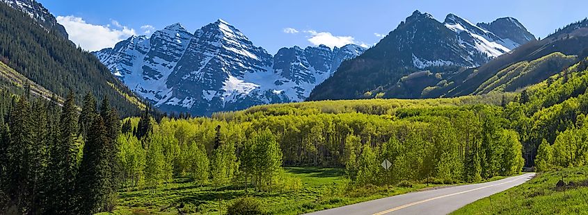 Panoramic view of Maroon Bells rising in the green Maroon Creek Valley, as seen from Maroon Creek Road on a sunny spring evening in Aspen, Colorado.