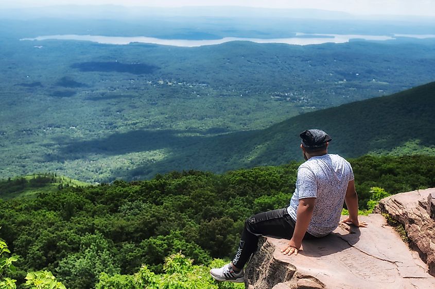 A man sitting on the edge of a cliff on top of the Overlook Mountain in the Catskills in Woodstock, New York. Editorial credit: Dan Hanscom / Shutterstock.com