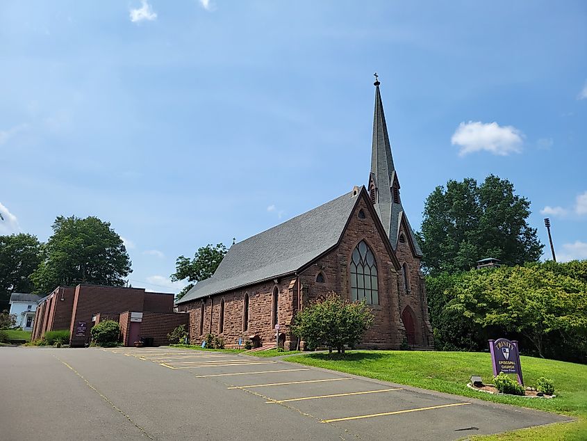 Trinity Episcopal Church in Tariffville, Connecticut, a historic stone church with Gothic-style architecture, arched windows, and a tall steeple, surrounded by trees.