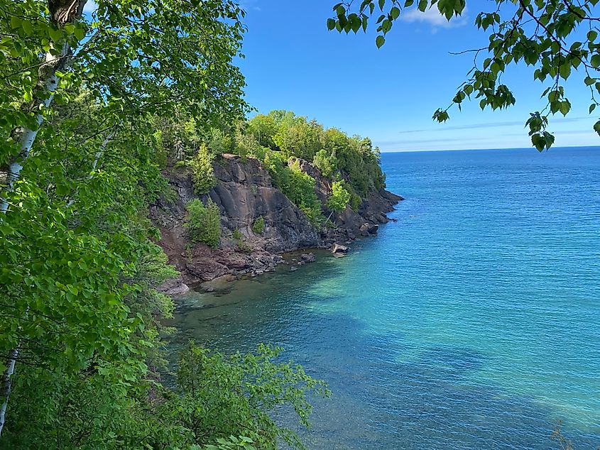 A sheer, forested cliff meets the pristine waters of Lake Superior on a sunny afternoon