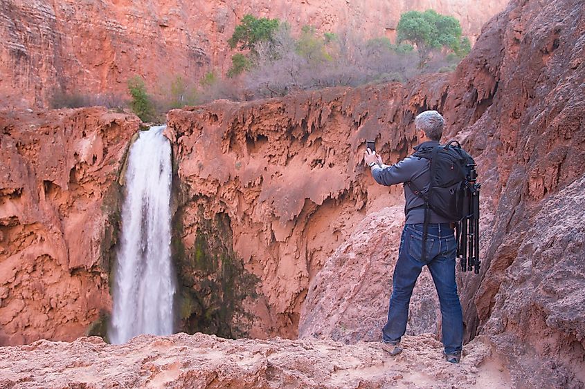 A man with photo gear takes picture of Mooney Falls with his mobile phone, Havasu Canyon, Arizona