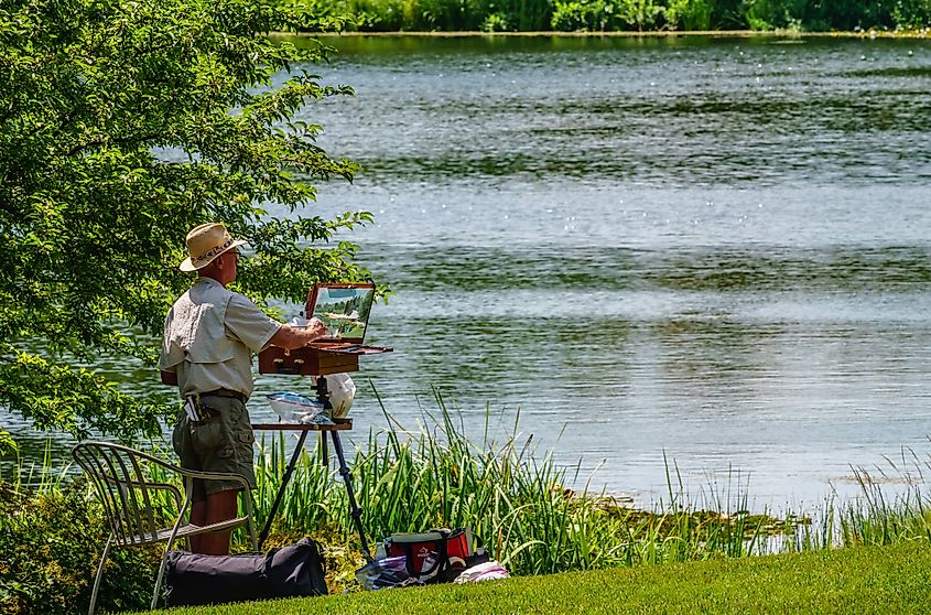 GLENCOE, ILLINOIS/USA - AUGUST 8, 2019: A senior watercolor artist stands painting a scene by a quiet lagoon on a sunny day at Chicago Botanic Garden.