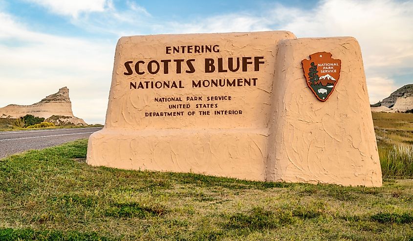 Stone entrance sign for Scotts Bluff National Monument with National Park Service emblem. Scenic bluffs and open sky in the background.
