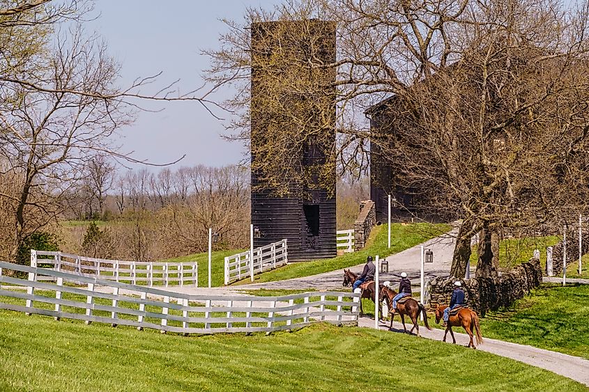 Three adult riders follow a scenic trail toward a historic barn at Shaker Village of Pleasant Hill in Harrodsburg, Kentucky