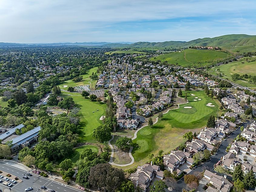 Aerial drone photos of the Oakhurst neighborhood in Clayton, California, featuring green hills, a golf course, and residential homes.