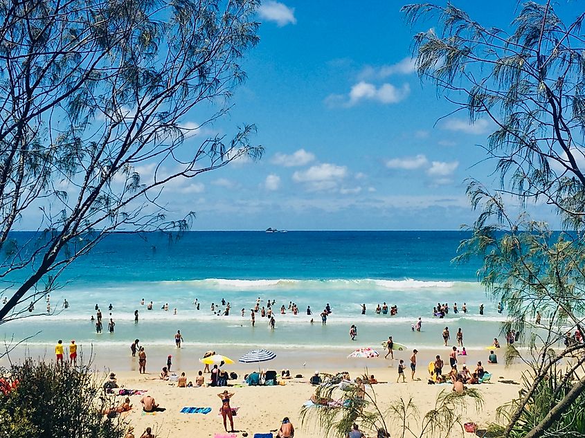 Horizontal Seascape of people enjoying the summer sun on busy tourist beach holiday with sand turquoise waves blue sky at famous surf ocean Byron Bay Australia