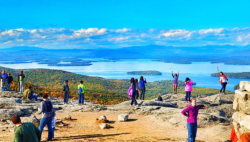 Tourists posing for photos at the summit of Mount Major. Lake Winnipesaukee and the Belknap Mountains in the background. Editorial credit: Helioscribe / Shutterstock.com