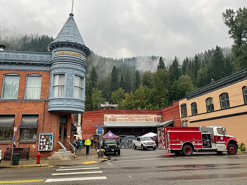 A fire truck blocks off a a street in historic Wallace, Idaho. Misty, forested mountains make up the background. 