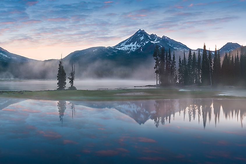 South Sister and Broken Top reflected in calm waters of Sparks Lake with morning mist rising into trees in the Cascades Range, Central Oregon