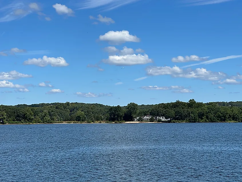 View across the Connecticut River from Chester, Connecticut showing calm water, a wooded shoreline, and a few houses beneath a sky with scattered clouds.
