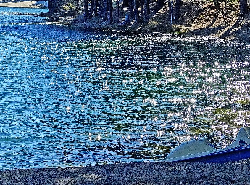 A paddle boat waits for a rider on the shore of Green Valley Lake in the San Bernardino Mountains. The early morning sun reflects off the waves like diamonds. All is quiet.