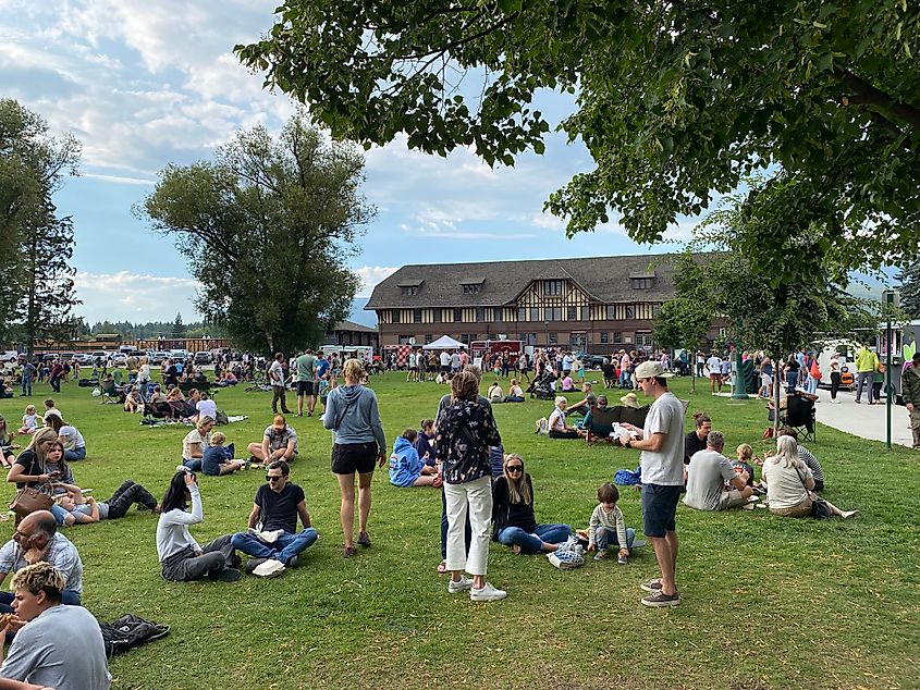 A crowd casually gathers in a park outside of a train depot.