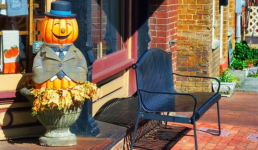 A happy jack-o-lantern statue adorns the steps leading into a store on main street.