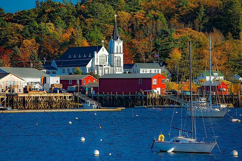 Our Lady Queen of Peace Catholic Church on the shore of Boothbay Harbor, Maine, with sailboats moored in the harbor.