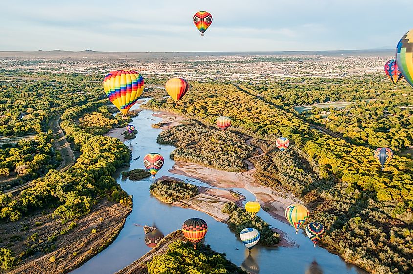 Hot air balloons floating above the Rio Grande, with vibrant colors reflecting on the river's surface.