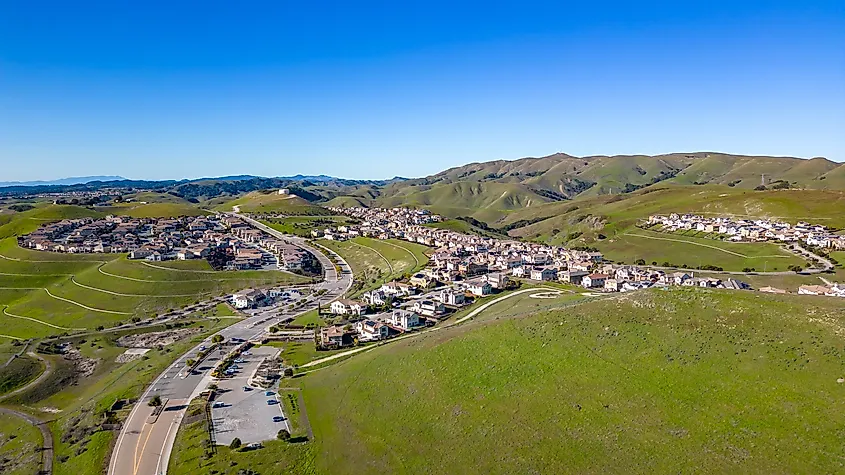 Aerial images over the green hills in Dublin, California with Real Estate in the background and a blue sky.