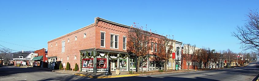 Charming downtown street in Corydon, Indiana, featuring historic brick buildings adorned with festive decorations, small businesses, and a clear blue sky.