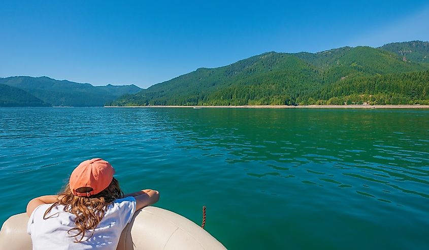 A girl wearing a cap looks out from a boat at Detroit Lake shoreline in Oregon.