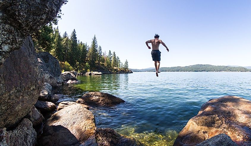 Young man jumping off a rocky cliff in Tubs Hill in to Coeur d' Alene Lake in Northern Idaho