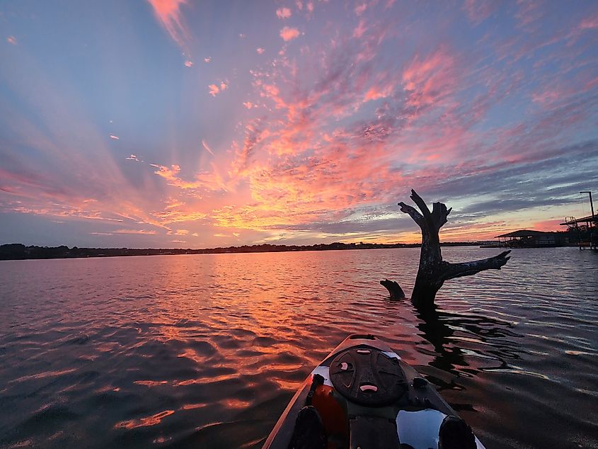 The beautiful Lake Granbury in Texas with a kayak in foreground leading to a sunset sky.