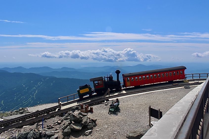 The Mount Washington Cog Railway at the summit, with its historic train and tracks set against the rugged terrain and expansive views. 