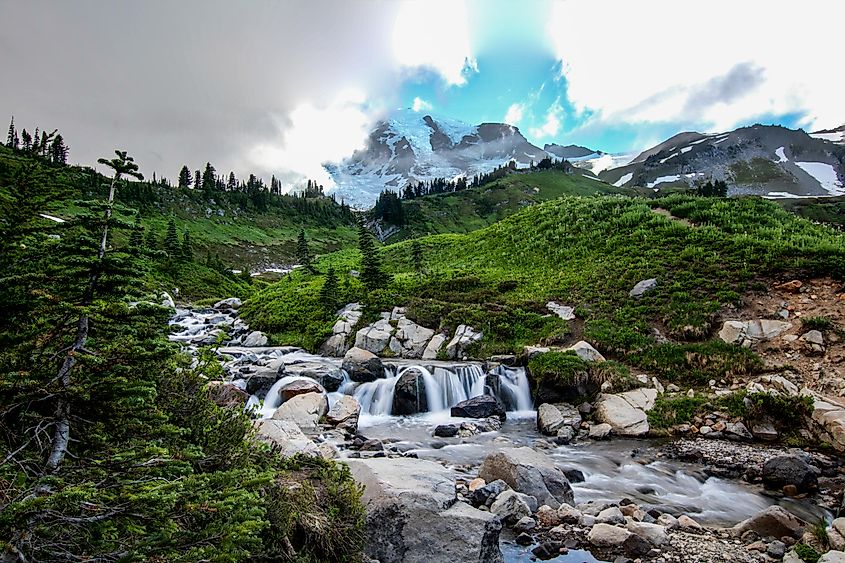 A cascade in Edith Creek just above Myrtle Falls. The summit of Mount Rainier can be seen just behind thick rain clouds rolling by.