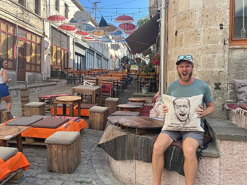 A man making a funny face in imitation of Charles Bukowski (who is featured on the pillow he's holding).