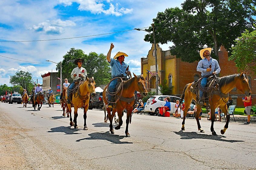 Cowboys enjoying hot dogs and drinks while riding in the annual Flint Hills Rodeo parade in Strong City, Kansas.