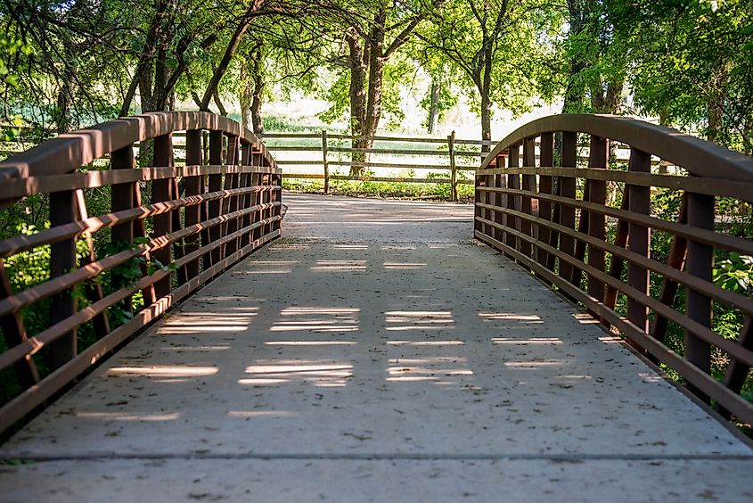 A pedestrian bridge over a small creek at Keller Pointe Park in Keller, Texas that leads to an open field.