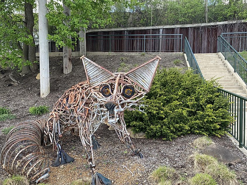 A metal fox sculpture stands beside a pedestrian river bridge 