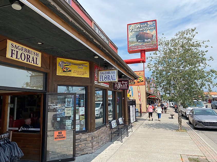 A West Yellowstone visitor's sign with a large bison stands above a shop-lined street. 