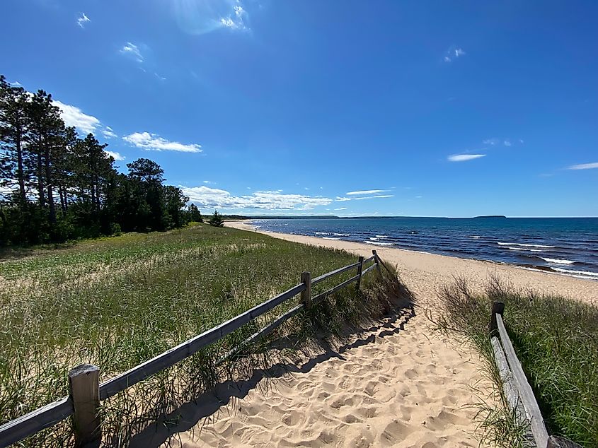 A roadside turnout leading to an empty sandy beach pinched between Lake Superior and a bordering forest