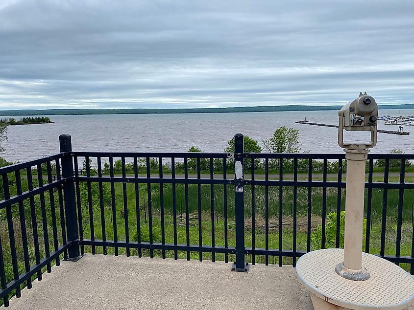 Mounted binoculars atop an observation deck overlook a verdant bay and a small marina.
