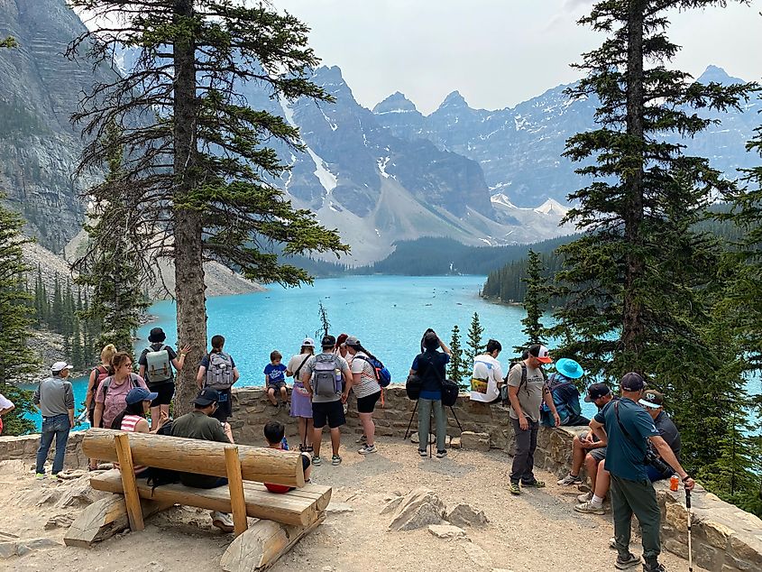 A crowd gathers at a viewpoint above a turquoise mountain lake.