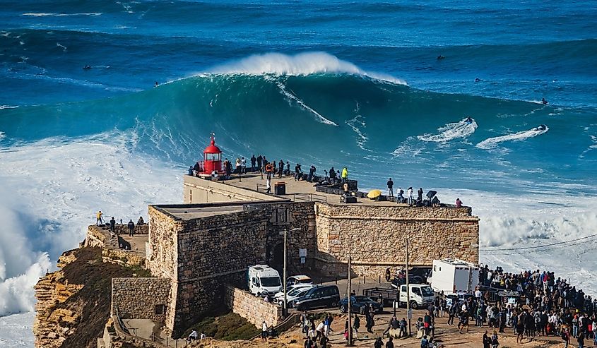 Surfer riding huge wave near the Fort of Sao Miguel Arcanjo Lighthouse in Nazare, Portugal. Nazare is famously known for having the biggest waves in the world.