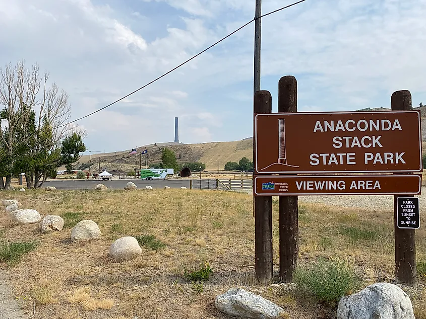 A sign for Anaconda Stack State Park stands before the hilltop smokestack seen in the distance.