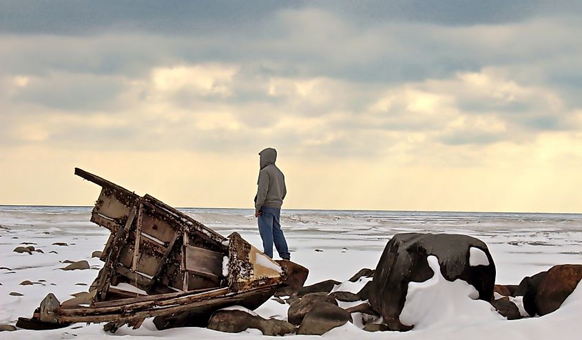An adolescent male looking out over a desolate Lake Huron with a shipwreck in the foreground.