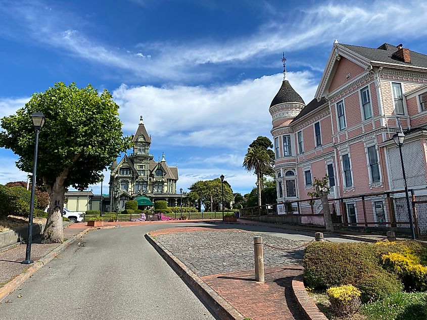 A pink mansion faces another ornate Victorian mansion across the street.