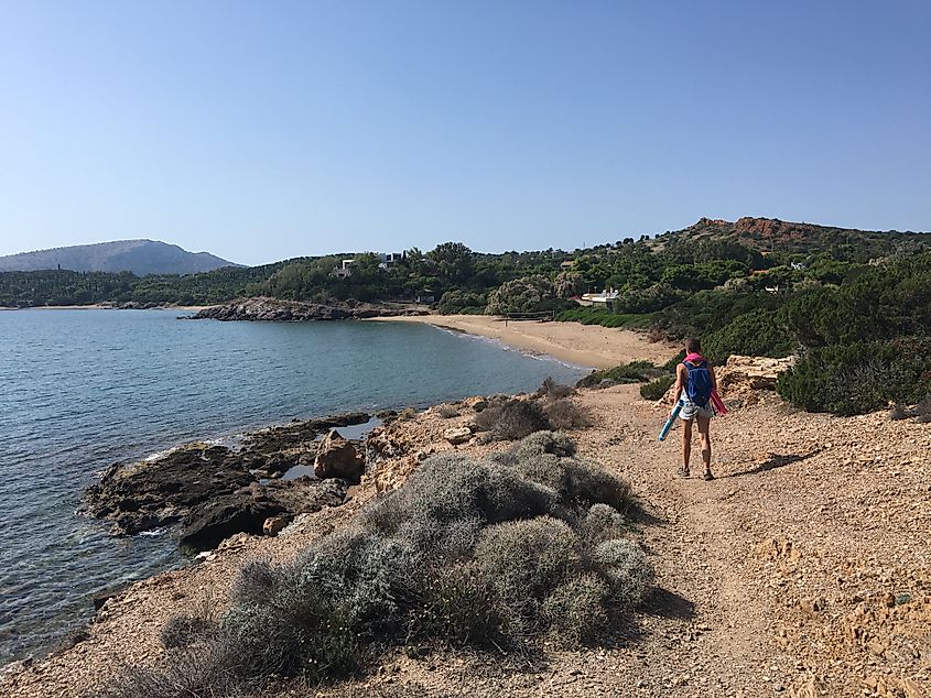 A woman with towel and yoga mat hikes a gentle shoreline trail toward an empty beach.