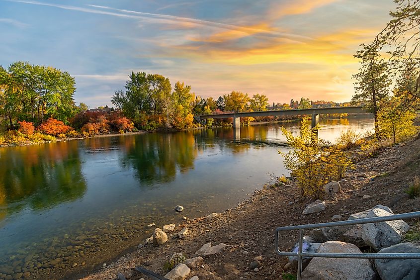 Sunset over the Spokane River at the Islands Trailhead along the Centennial Trail, with warm colors reflecting on the water and trees lining the riverbank in Spokane, Washington.