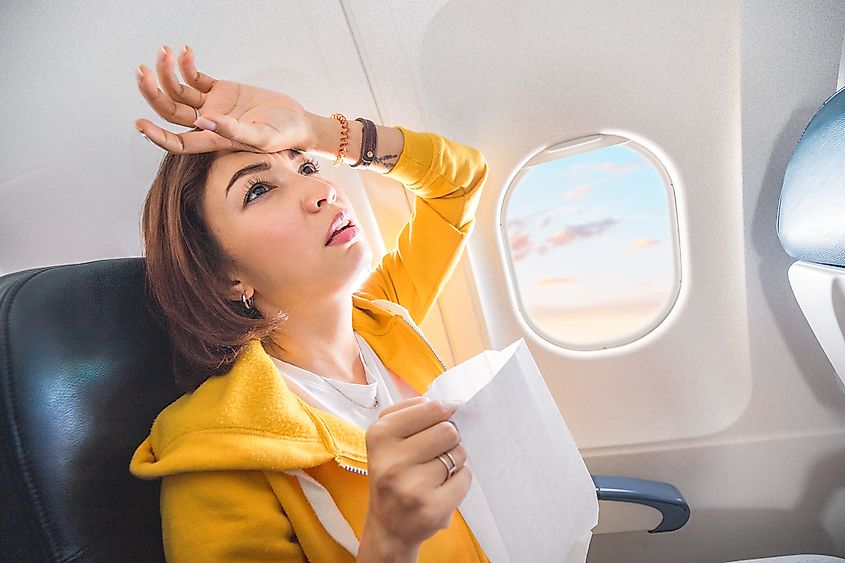 An Asian female traveler experiences acute nausea during turbulence on a plane. The woman feels seasick and airsick during the flight.