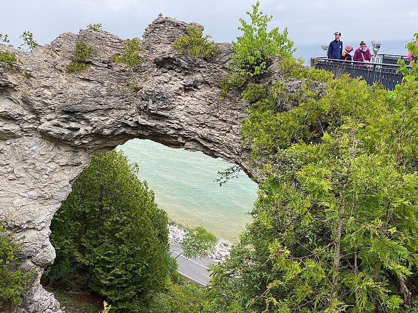 A family stands atop a lookout platform beside Arch Rock on Mackinac Island. The perimeter cycling road can be seen through the gap. 