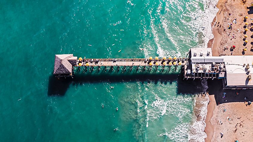 Aerial view of the Cocoa Beach Pier in Florida, with the clear blue sea surrounding it.