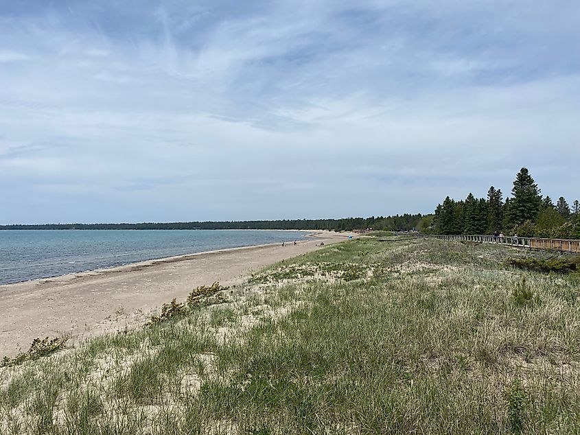 An empty lake beach paralleled by dune grasses and a boardwalk stretch off into the distance.