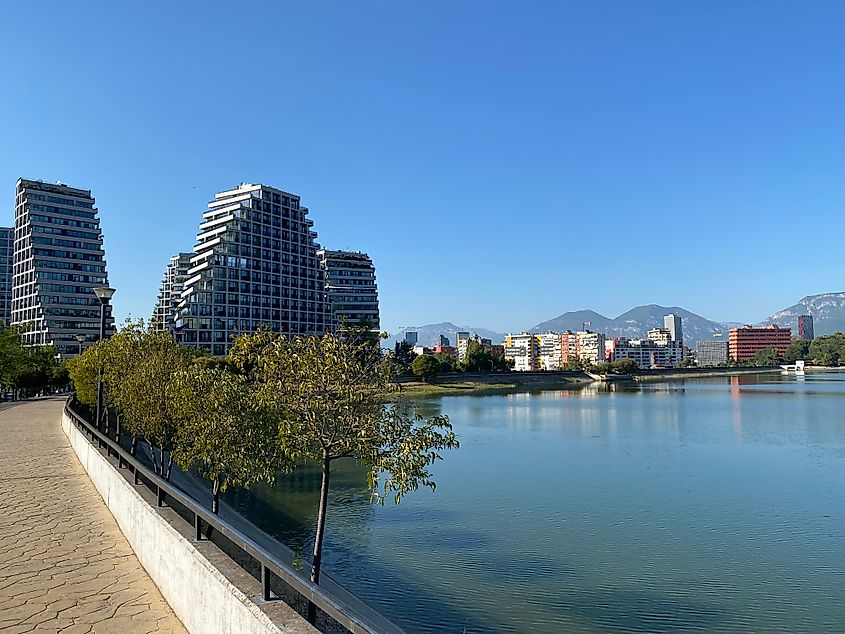 A tranquil city park with paved walking path, large lake, and mountains in the backdrop.