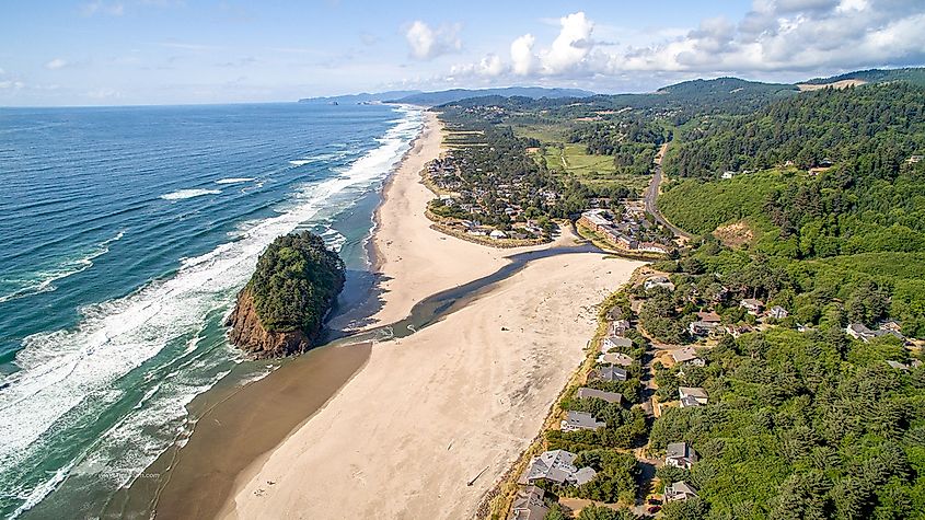 Aerial view of Neskowin, showcasing Proposal Rock surrounded by ocean waves and the Salmon River winding through the landscape.